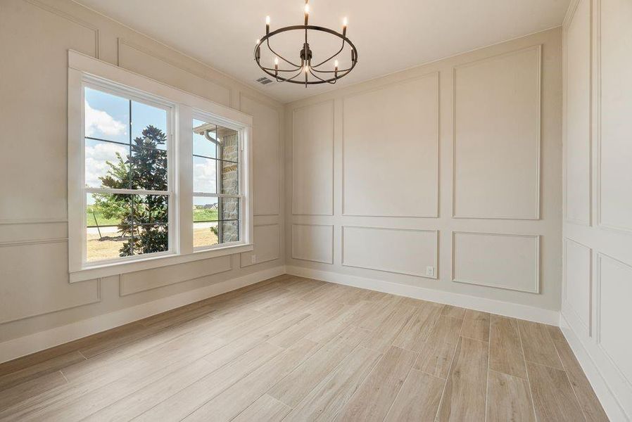 Unfurnished room featuring a decorative wall, suspended lighting, and wood tiled floors