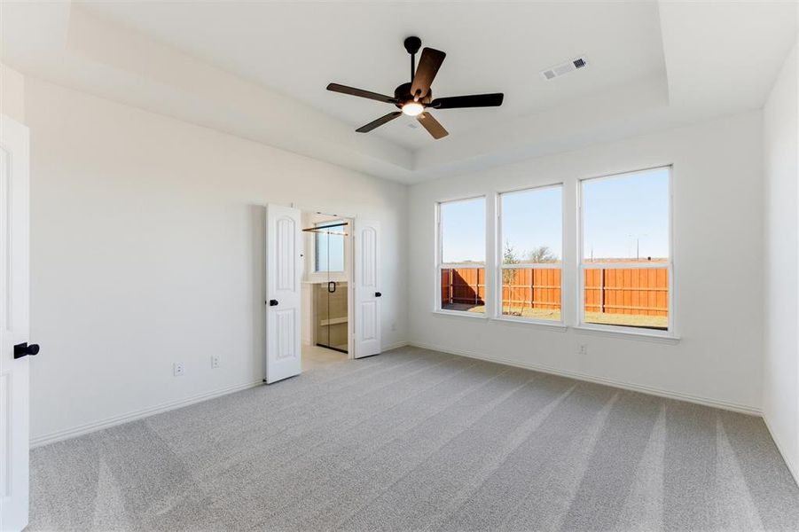 Unfurnished bedroom with a raised ceiling, ceiling fan, and light colored carpet