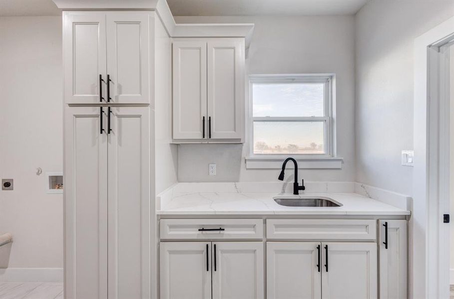 Kitchen featuring white cabinets, light stone counters, and sink