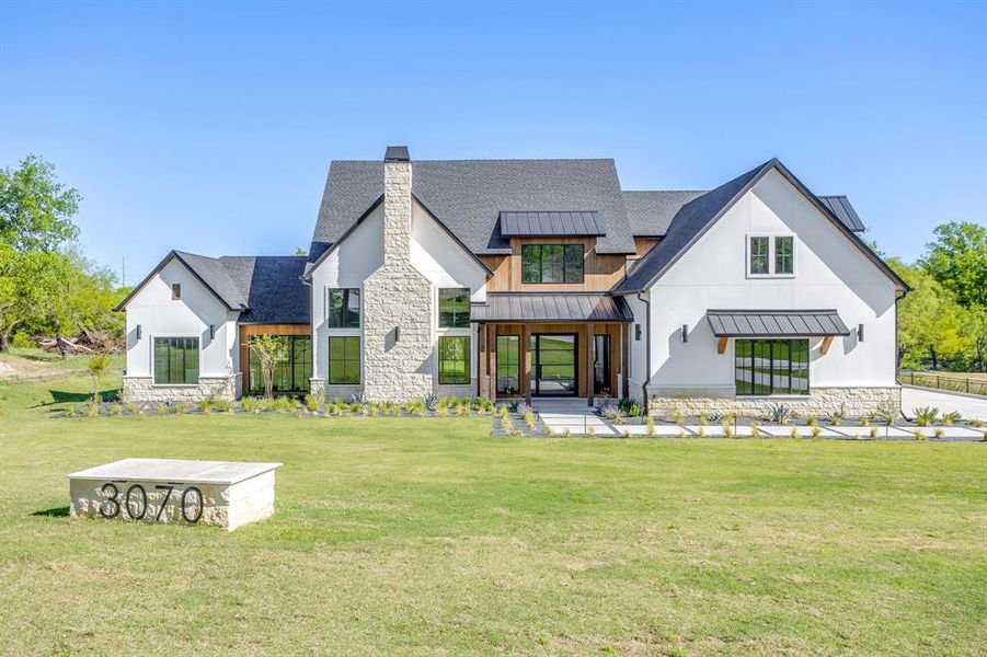 Rear view of house with a standing seam roof, stone siding, a lawn, and a chimney
