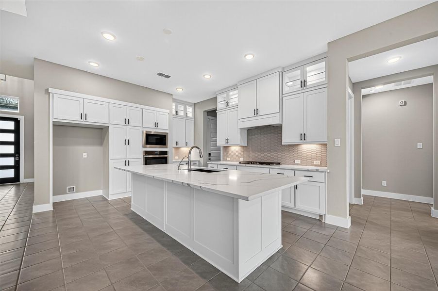 Kitchen with an island large enough for barstool seating, undermount lighting, stainless steel appliances, and lighted display cabinets across the top of the cabinets.