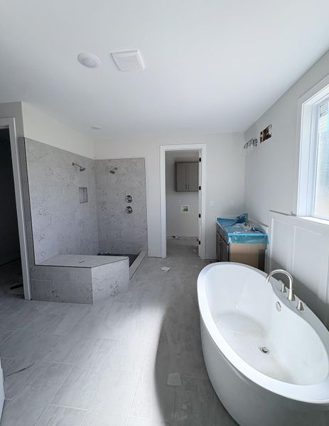 Spacious bathroom featuring a freestanding soaking tub, large tiled shower with dual showerheads, and light gray-toned floor tiling Spacious bathroom featuring a freestanding soaking tub, large tiled shower with dual showerheads, and light gray-toned floor tiling