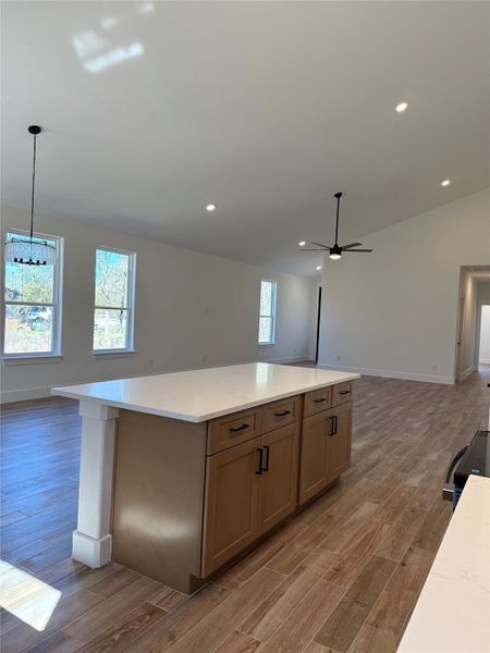 Kitchen featuring open floor plan, lofted ceiling, hanging light fixtures, a kitchen island, and light wood-style flooring