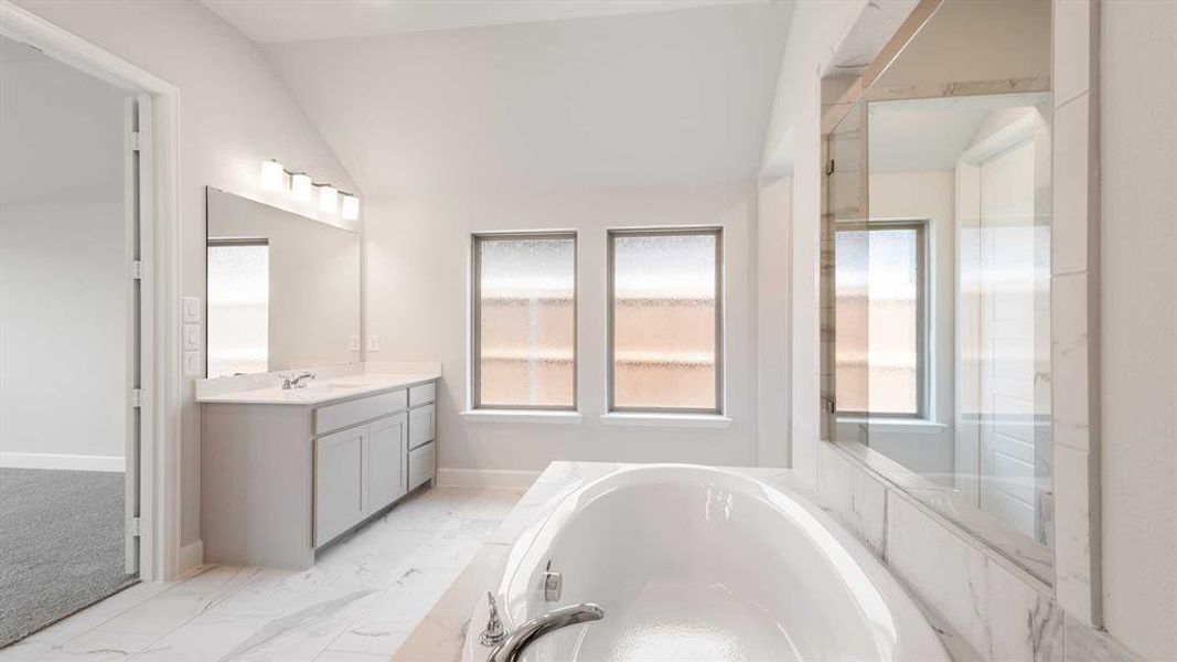 Bathroom featuring vanity, tiled bath, tile patterned floors, and vaulted ceiling