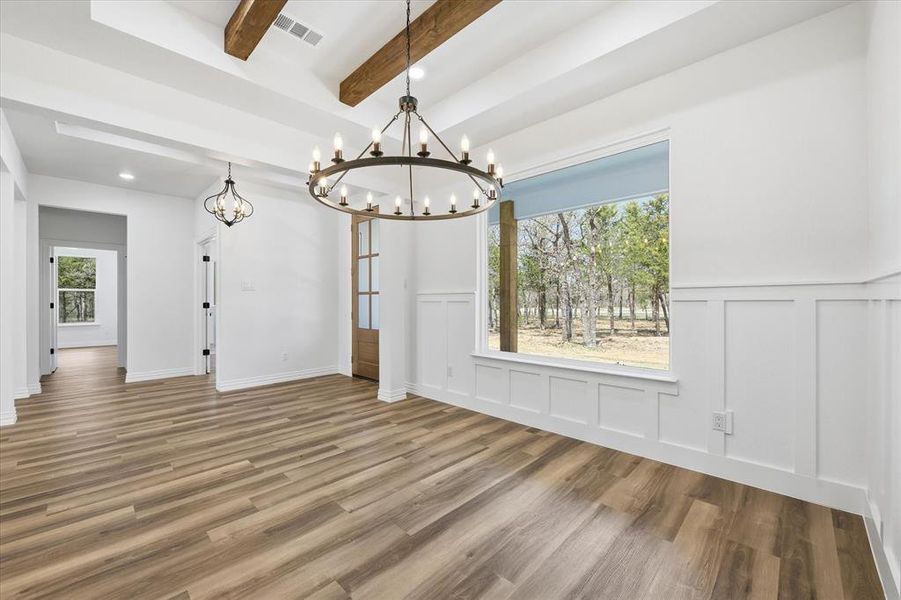Unfurnished dining area featuring a wainscoted wall, a decorative wall, wood finished floors, beamed ceiling, and hanging lights