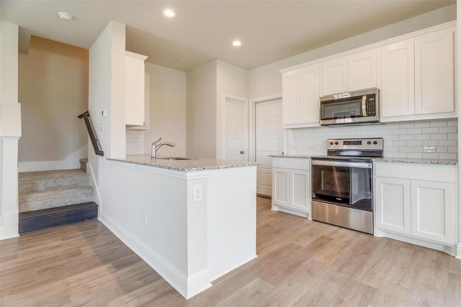 Kitchen featuring backsplash, stainless steel appliances, light stone counters, white cabinets, and recessed lighting