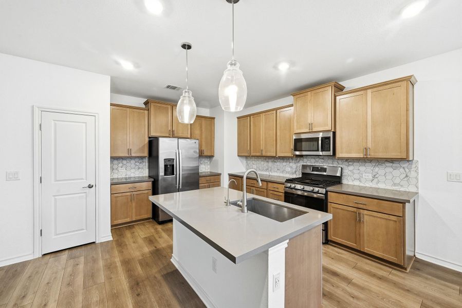 Kitchen featuring stainless steel appliances, an island with sink, decorative light fixtures, light wood-type flooring, and tasteful backsplash