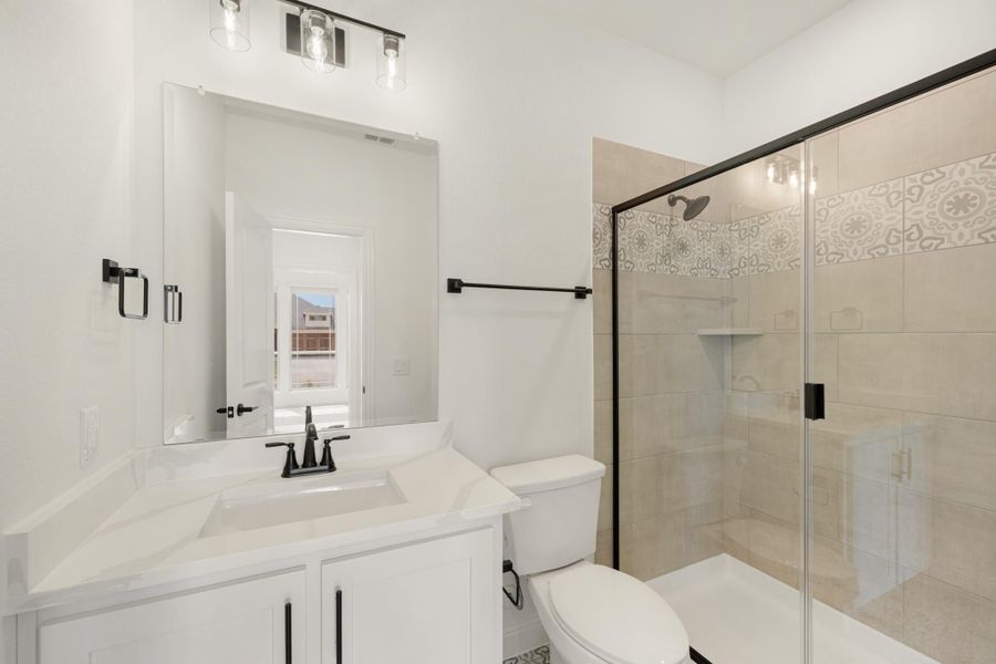 Bathroom with white vanity, walk-in glass shower with decorative tile, and black hardware accents