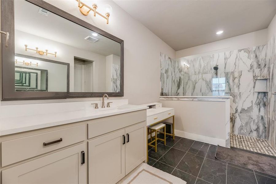 Spacious bathroom featuring a double vanity with white countertops, a large framed mirror, and a walk-in shower with marble-look tile surround