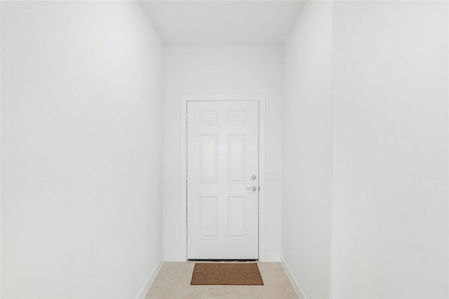 Narrow entryway with white six-panel door, small brown doormat, and light tile floor