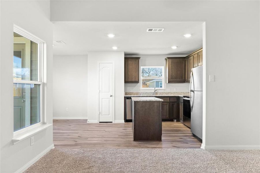 Kitchen with freestanding refrigerator, dark brown cabinets, a kitchen island, baseboards, and recessed lighting