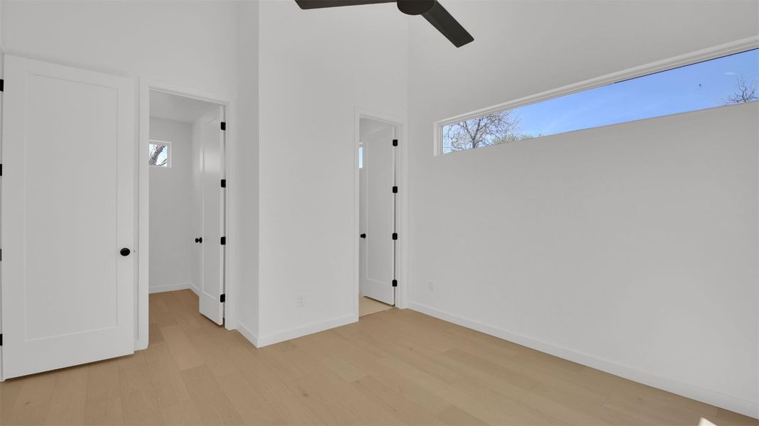 Bedroom featuring light wood-style floors, multiple windows, a high ceiling, and a ceiling fan