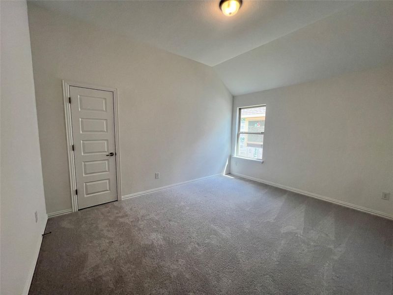 Carpeted empty room with vaulted ceiling and baseboards Carpeted empty room with vaulted ceiling and baseboards