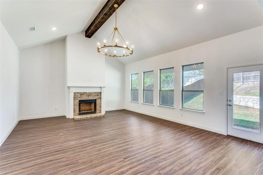 Unfurnished living room with dark wood-type flooring, beamed ceiling, plenty of natural light, and a brick fireplace