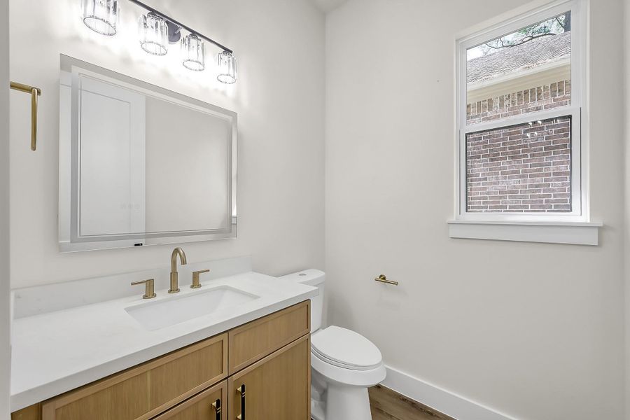 The powder room features natural wood tones and warm brushed gold hardware.