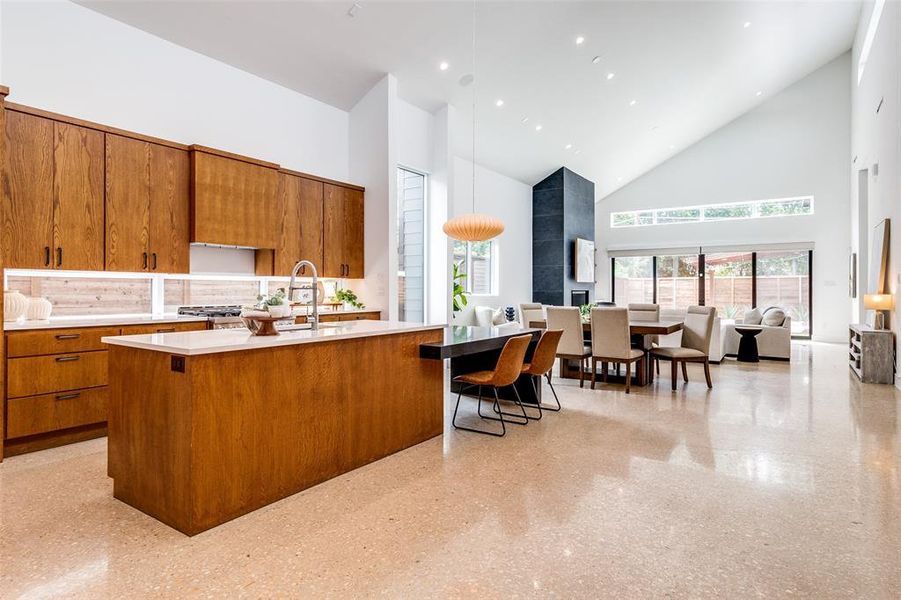 Kitchen featuring a breakfast bar, a center island with sink, decorative backsplash, and high vaulted ceiling