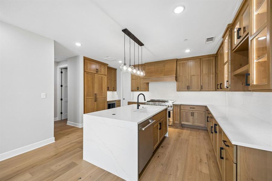 Kitchen with wood finish cabinets, light stone countertops, a center island with sink, tasteful backsplash, and stainless steel appliances Kitchen with wood finish cabinets, light stone countertops, a center island with sink, tasteful backsplash, and stainless steel appliances