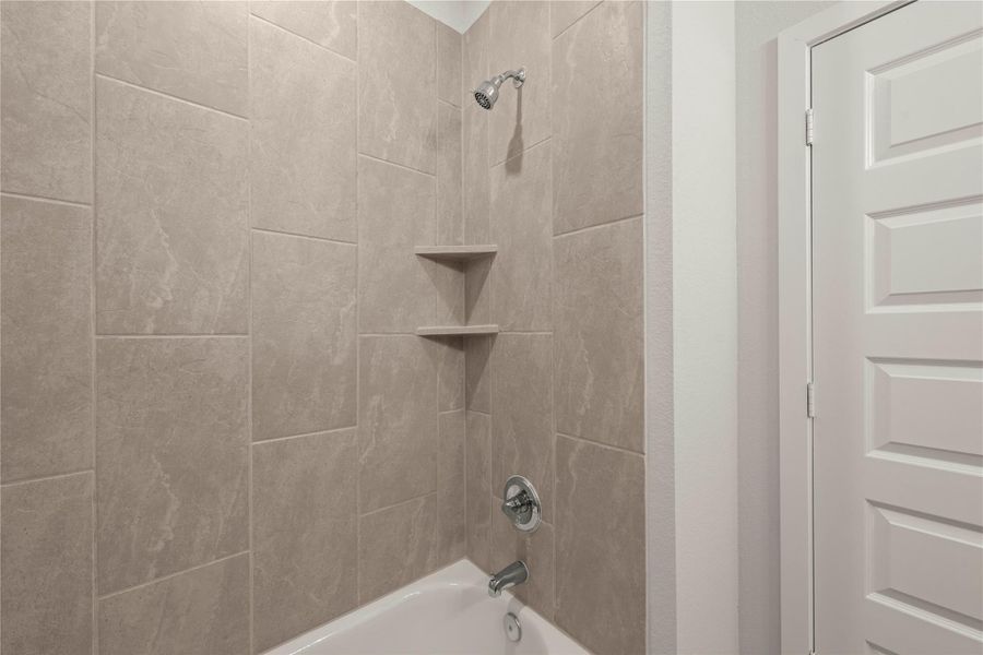 A well-appointed shower-over-tub in a primary bathroom with sleek tiled walls.