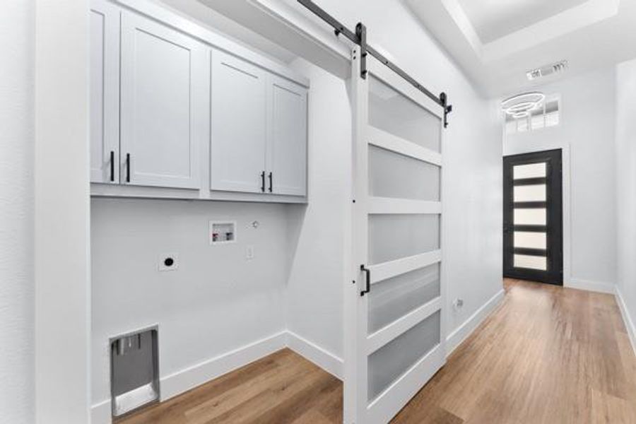 Laundry room with a barn door, light wood-style floors, hookup for a washing machine, cabinet space, and electric dryer hookup Laundry room with a barn door, light wood-style floors, hookup for a washing machine, cabinet space, and electric dryer hookup