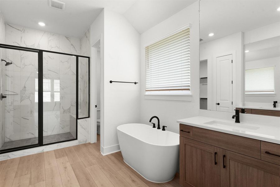 Contemporary bathroom featuring a freestanding soaking tub, a spacious walk-in shower with bench seating, a double vanity with ample storage, a large mirror, and wood-finish flooring Contemporary bathroom featuring a freestanding soaking tub, a spacious walk-in shower with bench seating, a double vanity with ample storage, a large mirror, and wood-finish flooring