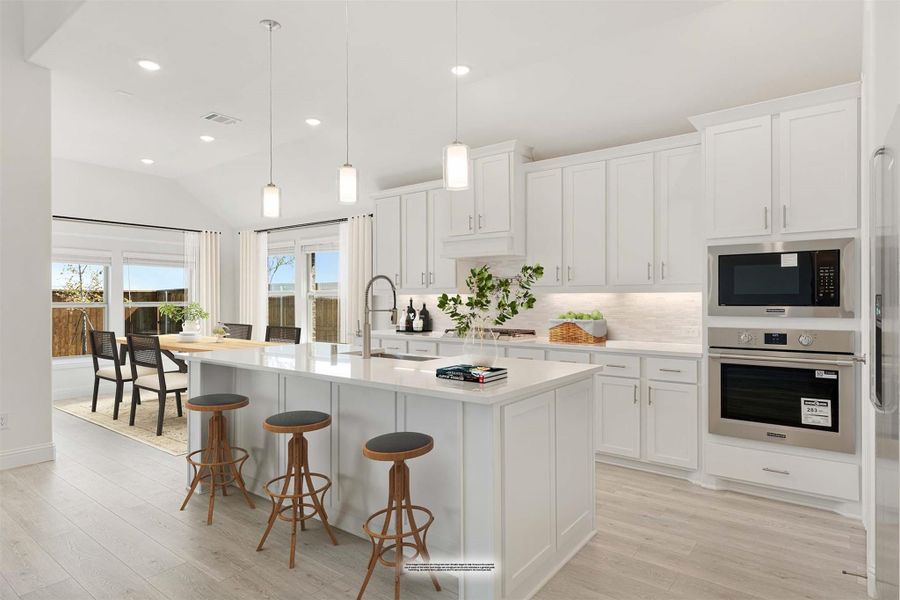 Open kitchen with white cabinets, large island with bar stools, stainless steel appliances, and light wood floors Open kitchen with white cabinets, large island with bar stools, stainless steel appliances, and light wood floors