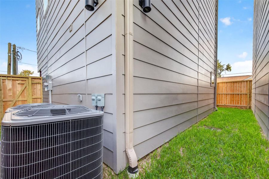 A private side yard with wood privacy fencing and green lawn provides low-maintenance outdoor space, a practical urban amenity in a neighborhood setting. The home's clean horizontal siding and exterior lighting are visible from this angle as well.