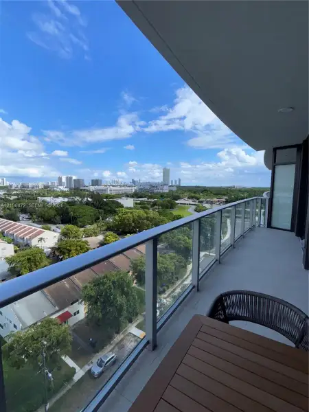 Covered balcony featuring a sleek glass railing and expansive urban and canopy scenery Covered balcony featuring a sleek glass railing and expansive urban and canopy scenery