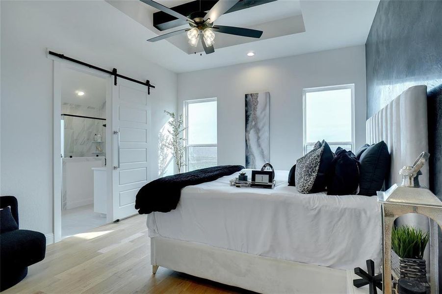 Bedroom with a barn door, wood finished floors, ceiling fan, and connected bathroom