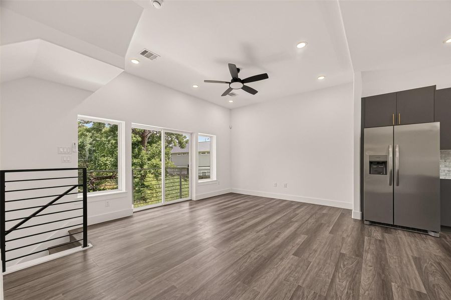This spacious, modern living area features sleek vinyl flooring, large windows for natural light, a ceiling fan, and an adjoining kitchen with stainless steel appliances. Perfect for open-concept living. This spacious, modern living area features sleek vinyl flooring, large windows for natural light, a ceiling fan, and an adjoining kitchen with stainless steel appliances. Perfect for open-concept living.