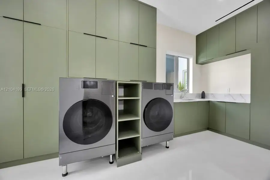 Full-height sage green cabinetry with matte black hardware, stone-surface backsplash, integrated shelving, and white tile flooring