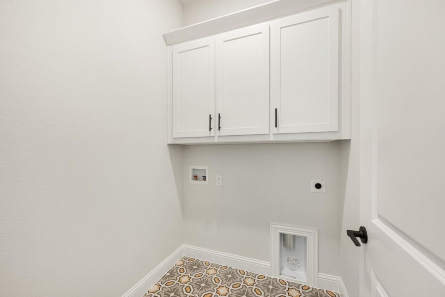 Laundry room with white upper cabinets, patterned tile floor, and washer and dryer hookups on the wall.