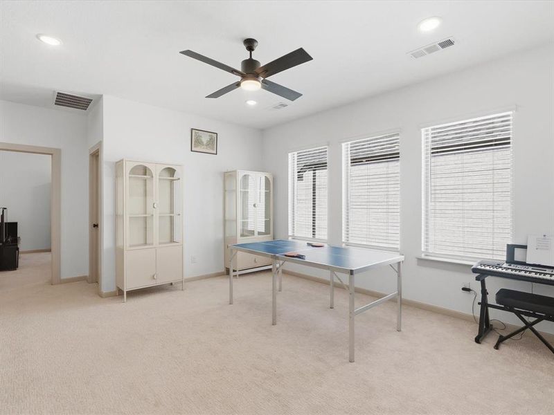 Spacious room featuring light-colored carpeting, multiple windows with blinds, a ceiling fan with integrated lighting, and recessed ceiling lights