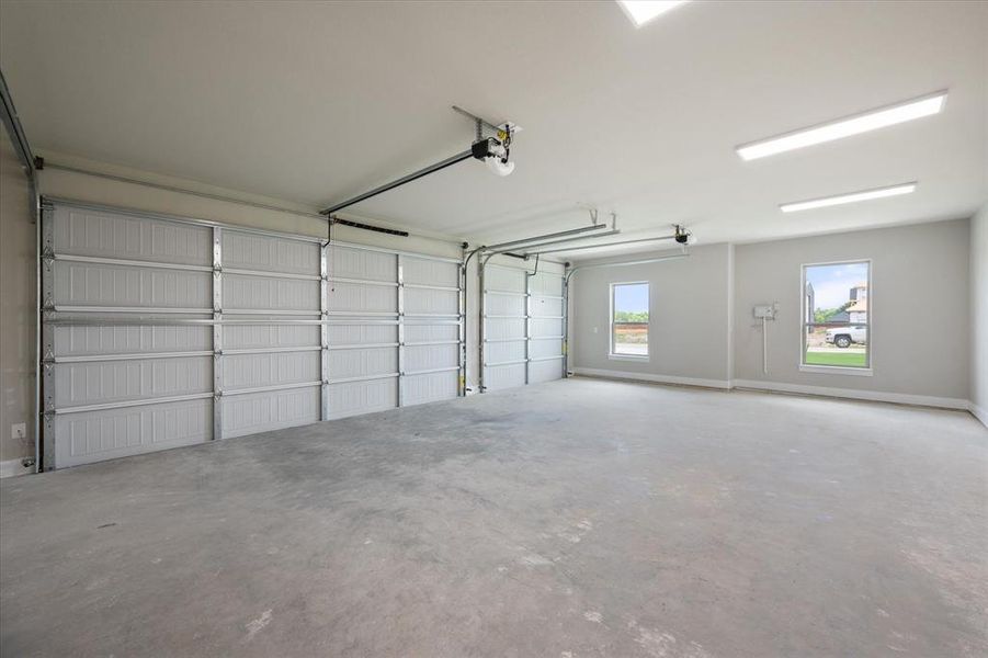 Spacious 3-car garage featuring two overhead doors, concrete flooring, overhead fluorescent lighting, and two windows providing exterior visibility