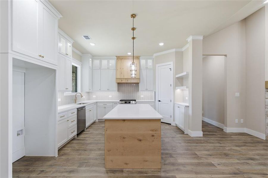 Open-concept kitchen featuring a central island with wood-finish paneling, white cabinetry, and light-toned countertops