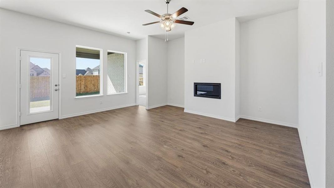 Open-concept living area featuring wood-finish flooring, a contemporary built-in fireplace, and a ceiling fan with integrated lighting Open-concept living area featuring wood-finish flooring, a contemporary built-in fireplace, and a ceiling fan with integrated lighting