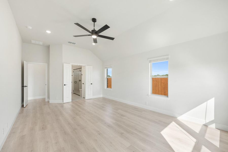 Spacious bedroom with vaulted ceiling, black ceiling fan, light wood floors, and ensuite bathroom entrance.
