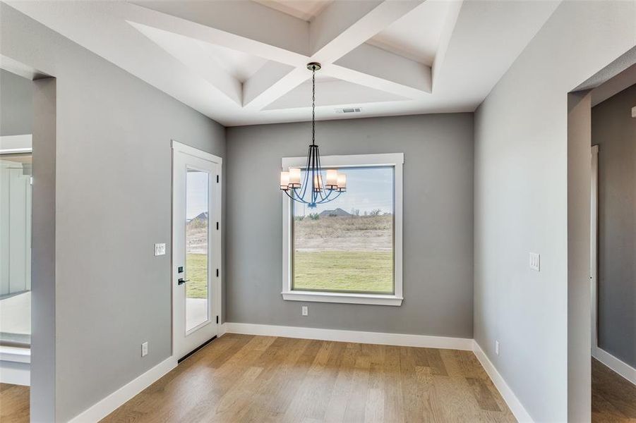 Unfurnished dining area featuring coffered ceiling, a chandelier, light wood-style flooring, and beam ceiling Unfurnished dining area featuring coffered ceiling, a chandelier, light wood-style flooring, and beam ceiling
