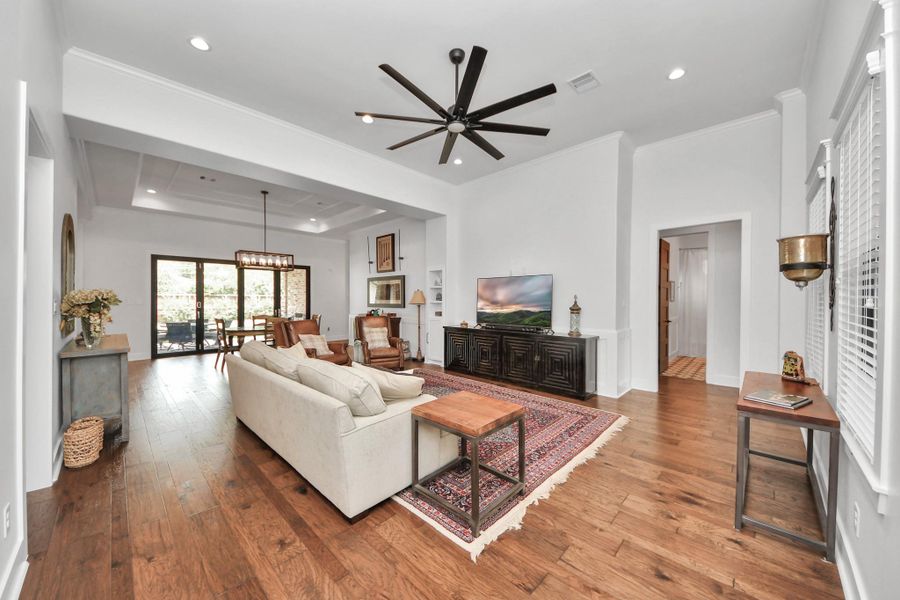 This spacious living area features hardwood floors, a modern ceiling fan, and ample natural light. It seamlessly connects to a dining area with large glass doors leading to an outdoor space, creating an inviting atmosphere perfect for entertaining.