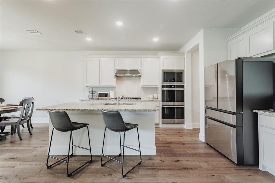 Kitchen featuring a large island with granite countertop, white cabinetry, stainless steel appliances, and wood-finish flooring