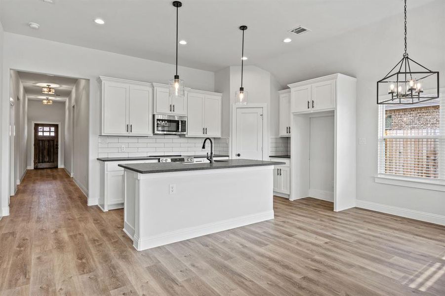 Kitchen featuring white cabinetry, stainless steel microwave, an island with sink, tasteful backsplash, and a chandelier