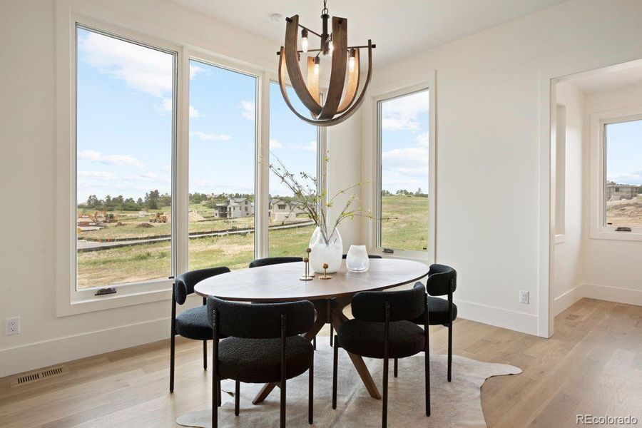 Sunlit dining area with expansive windows, contemporary chandelier, and sweeping views of the surrounding landscape.