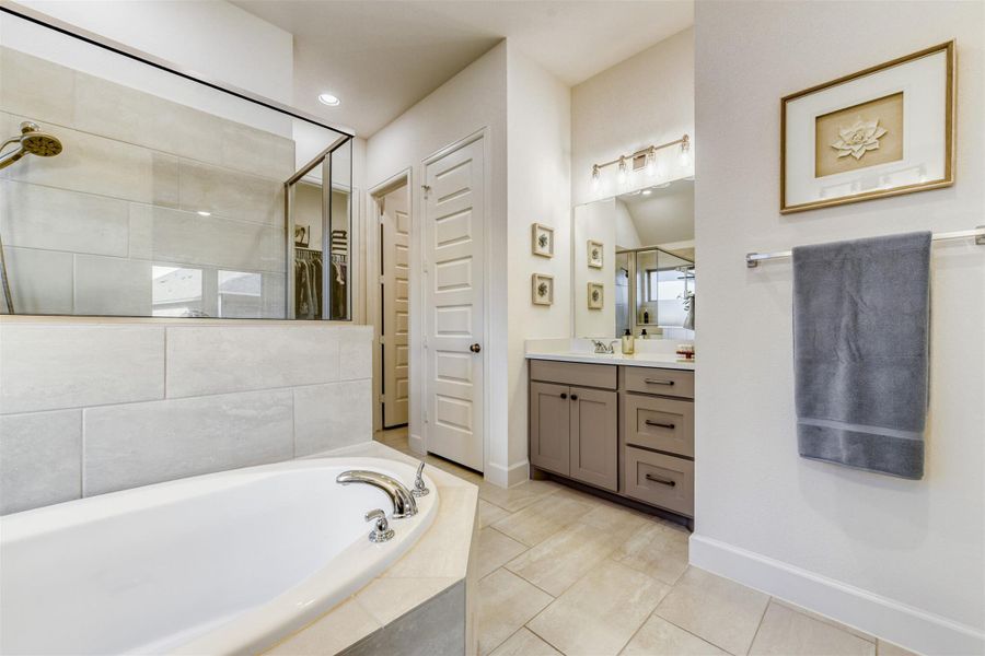 Full bath featuring a garden tub, vanity, light tile patterned floors, a tile shower, and a walk in closet