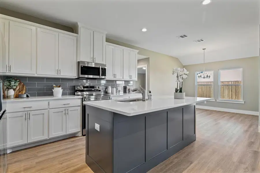 Kitchen featuring white cabinetry, sink, hanging light fixtures, backsplash, and appliances with stainless steel finishes