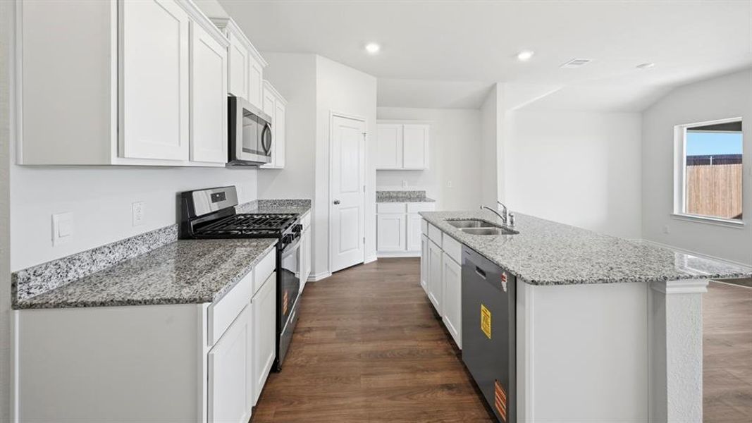 Kitchen featuring stainless steel appliances, light stone counters, white cabinetry, a center island with sink, and dark wood-style flooring