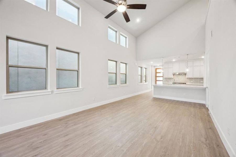 Unfurnished living room with high vaulted ceiling, light hardwood / wood-style floors, and ceiling fan