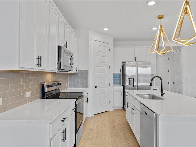 Kitchen featuring appliances with stainless steel finishes, an island with sink, light stone countertops, tasteful backsplash, and white cabinetry