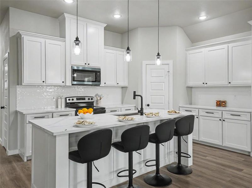 Kitchen featuring white shaker cabinetry, stainless steel appliances, a white tile backsplash, and wood-finish flooring Kitchen featuring white shaker cabinetry, stainless steel appliances, a white tile backsplash, and wood-finish flooring