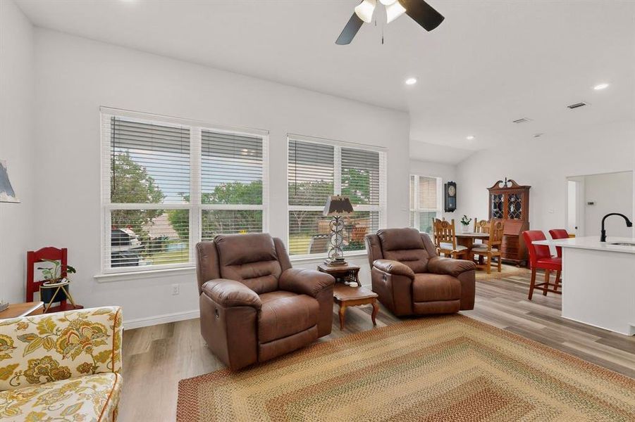 Bright living space featuring multiple windows with blinds, recessed lighting, a ceiling fan, and wood-finish flooring extending into the background