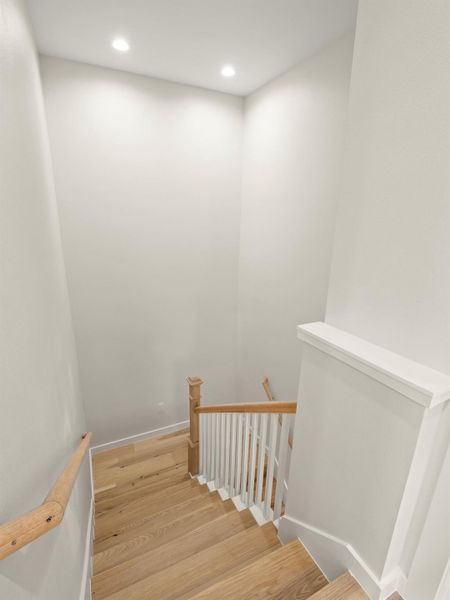 Staircase featuring wood-finish treads, a contrasting white baluster system, natural wood handrails, and recessed ceiling lighting