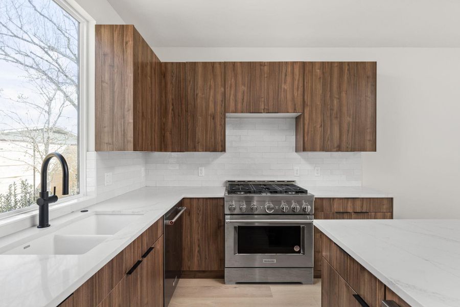 Kitchen with high end stove, dishwasher, light stone counters, modern cabinets, and a sink